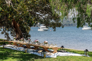 A charming picnic setup with low wooden tables and cushions by the water.