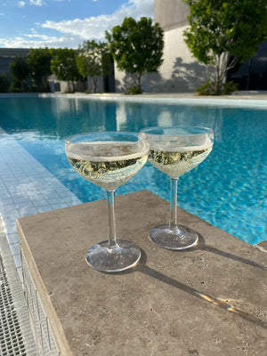 Two clear champagne coupes filled with sparkling white wine.